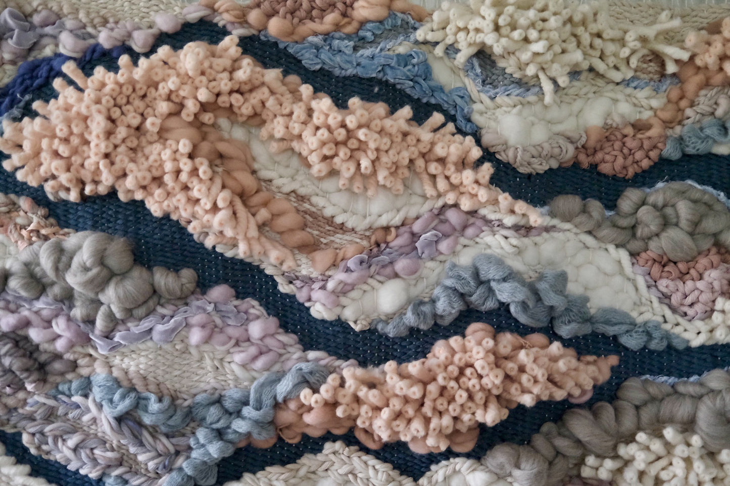 Contemporary woven wall art emphasizing softness and flow, handcrafted with sustainable fiber choices. Playful colors with shades of purple, pink, ivory, salmon, blue, and gray.