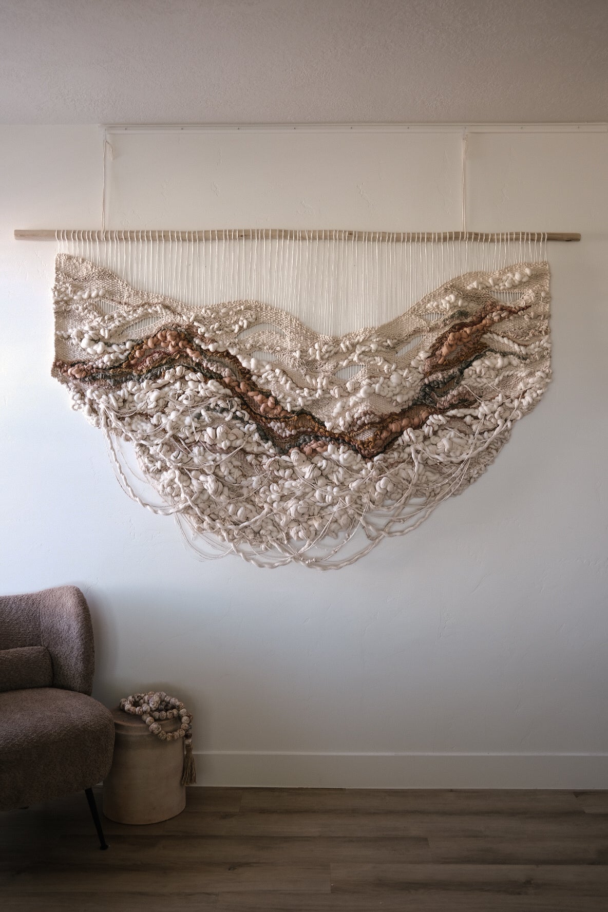 Abstract fiber art piece in calming beige and cream tones, created using cotton, wool, and recycled linen. hanging fringe, and knotted texture.