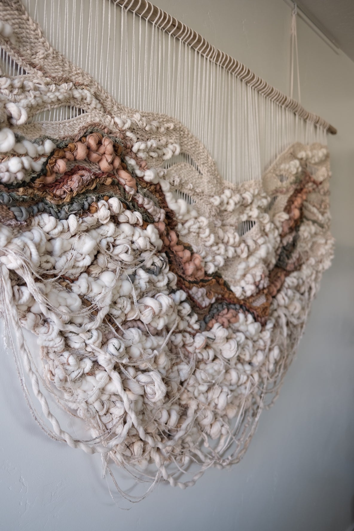 Abstract fiber art piece in calming beige and cream tones, created using cotton, wool, and recycled linen. Negative space, hanging fringe and knotted texture with organic shape.