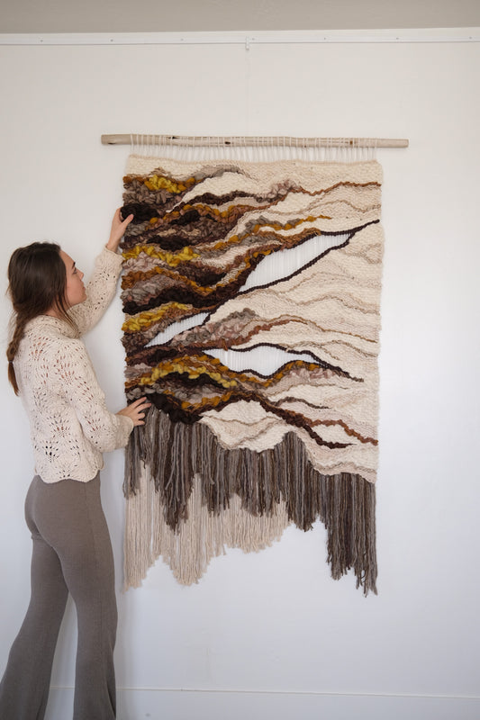 Neutral-toned woven wall hanging made from wool, cotton, and recycled linen, featuring layered textures and organic, flowing shapes, handcrafted by fiber artist Rebecca Whitaker.
