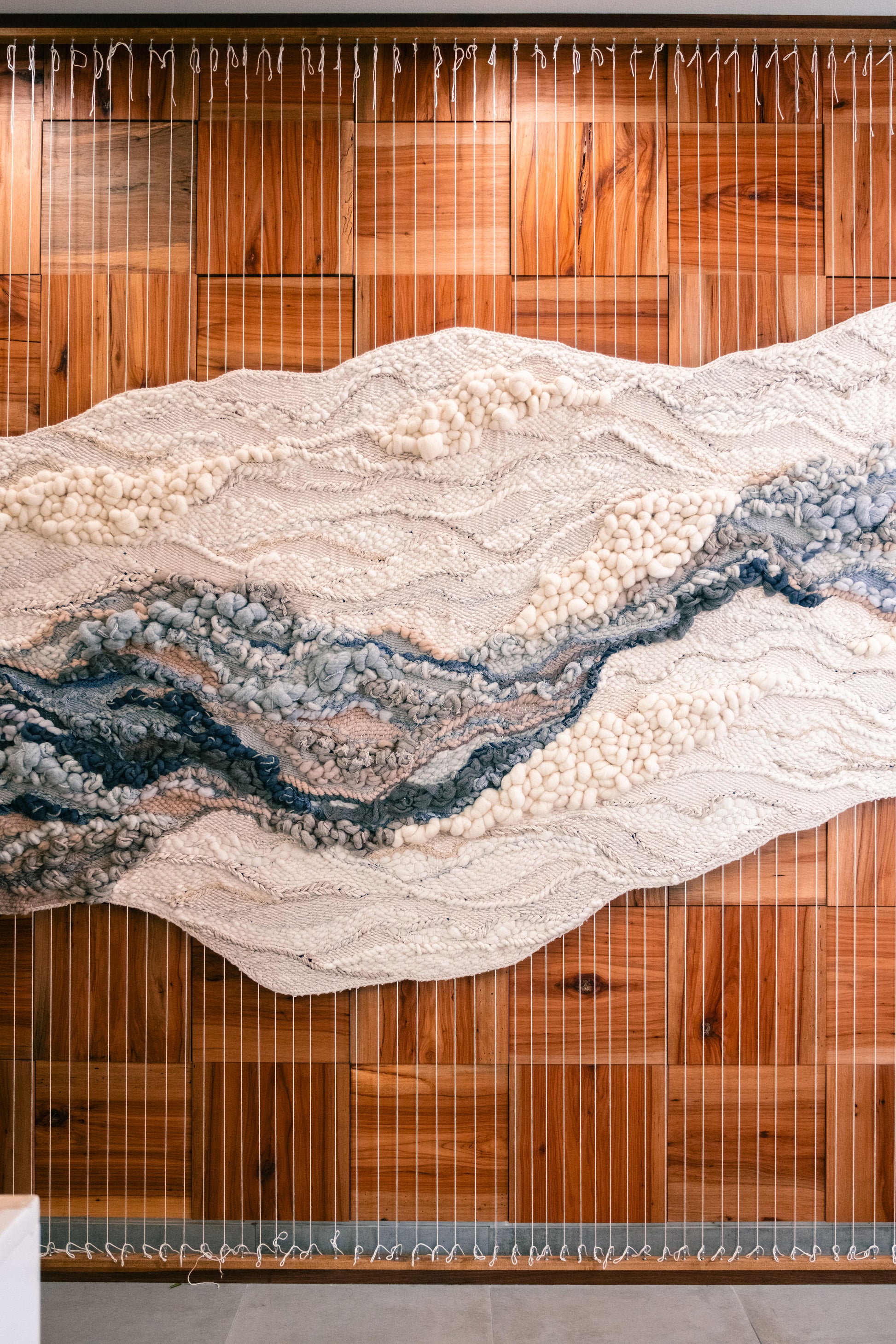 Modern woven wall hanging featuring soft, sculptural forms and a subtle palette of warm neutrals, blues and ivory.