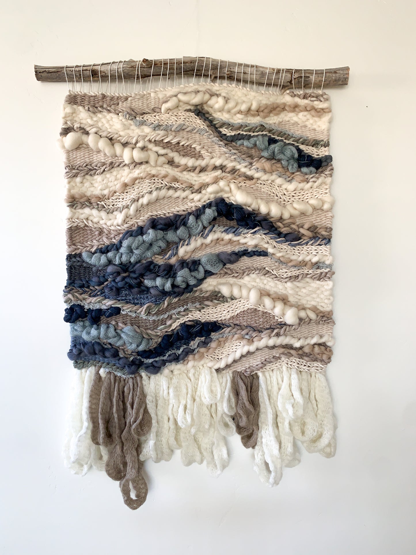Textural wall hanging inspired by coastal landscapes, featuring undulating patterns in soft blues and neutrals. Braided, knotted, bubbling and looping textures.