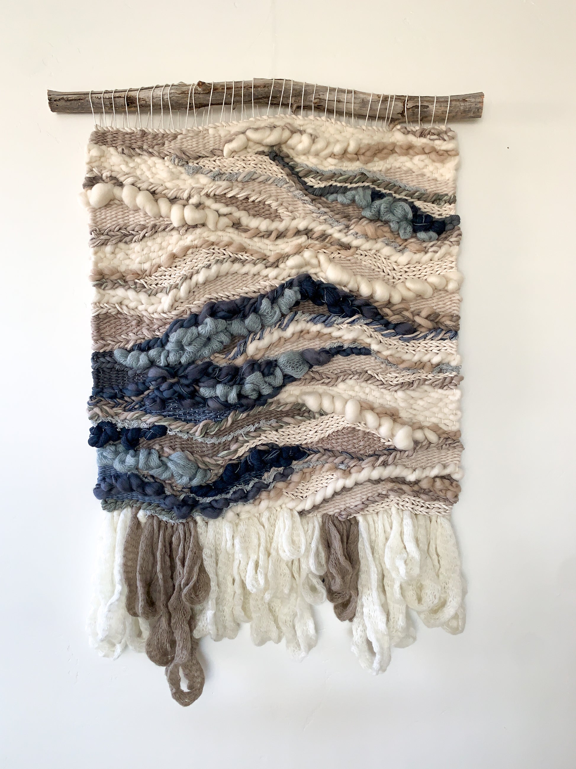 Textural wall hanging inspired by coastal landscapes, featuring undulating patterns in soft blues and neutrals. Braided, knotted, bubbling and looping textures.