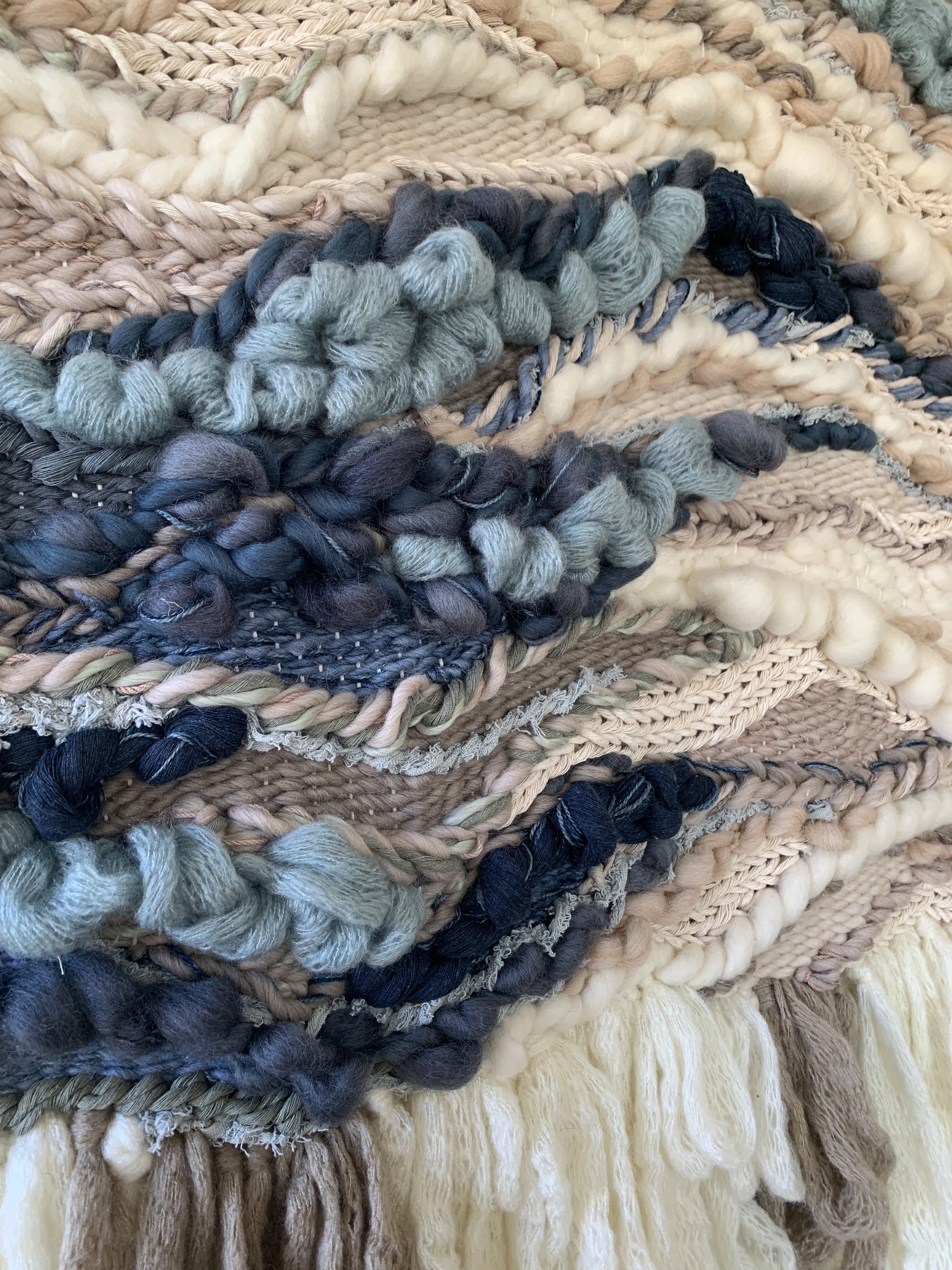 Textural wall hanging inspired by coastal landscapes, featuring undulating patterns in soft blues and neutrals. Organic flow and movement.