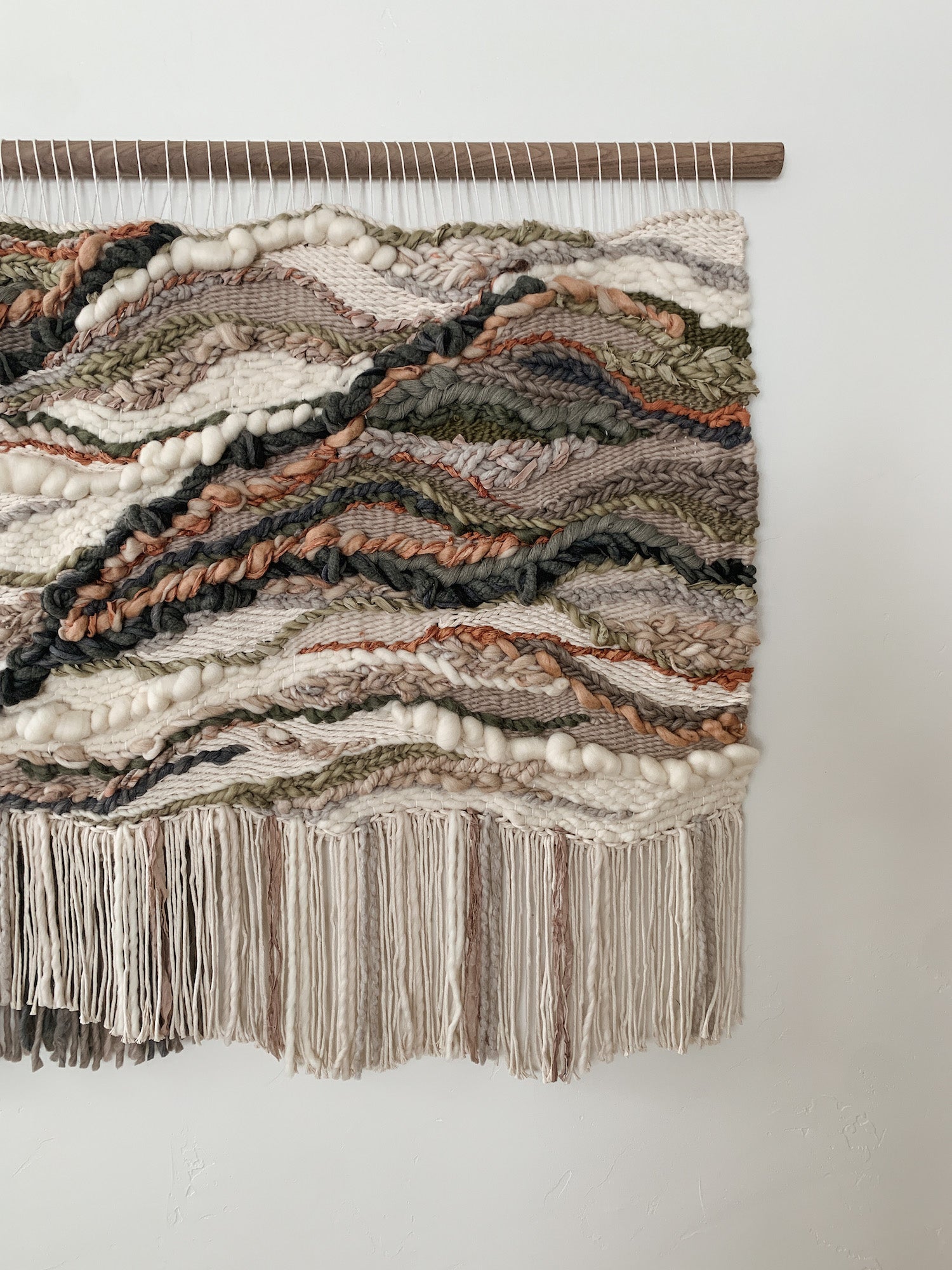 Soft fiber installation in muted tones, highlighting layered weaves and handcrafted movement. Accent colors in beige ivory, burnt orange, salmon, green, and browns.