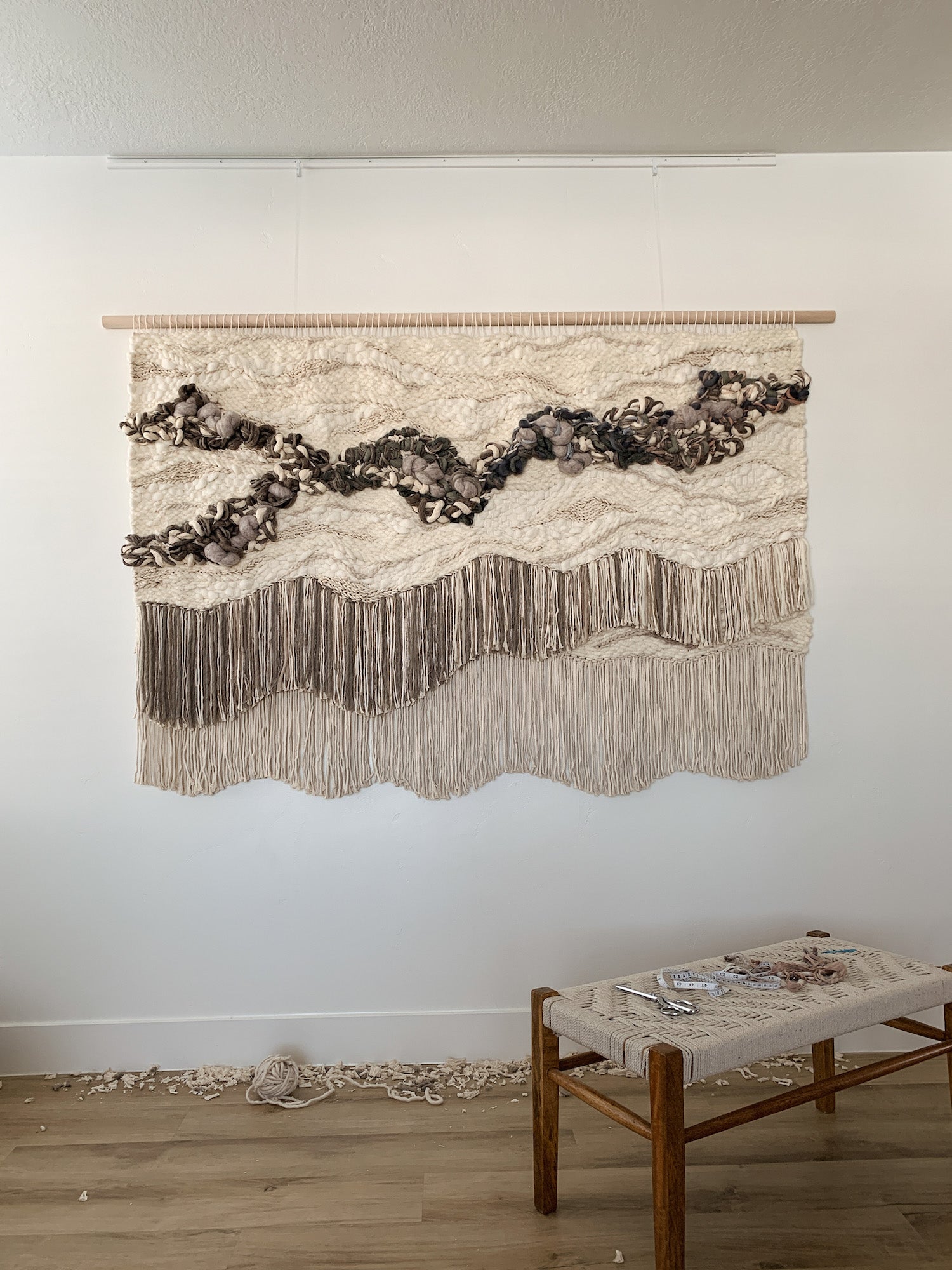 Wall-mounted fiber composition with cascading textures in soft, earthy palettes. Knotted textures with precise cut fringe incorporating organic and free movement.
