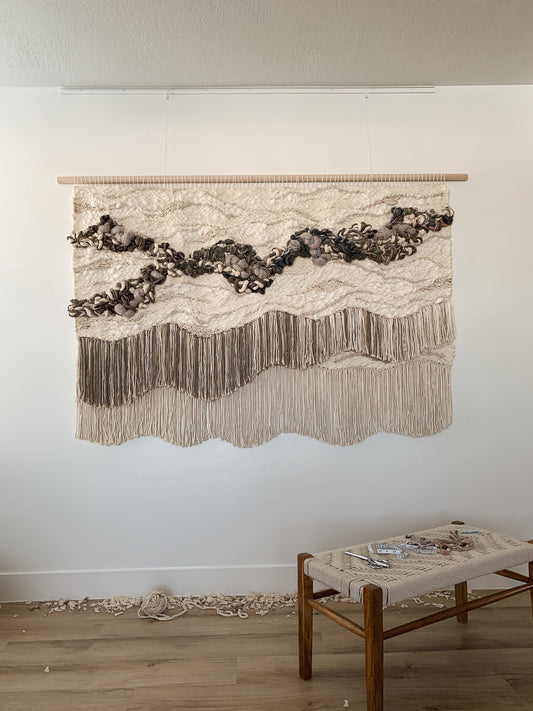 Wall-mounted fiber composition with cascading textures in soft, earthy palettes. Knotted textures with precise cut fringe incorporating organic and free movement.