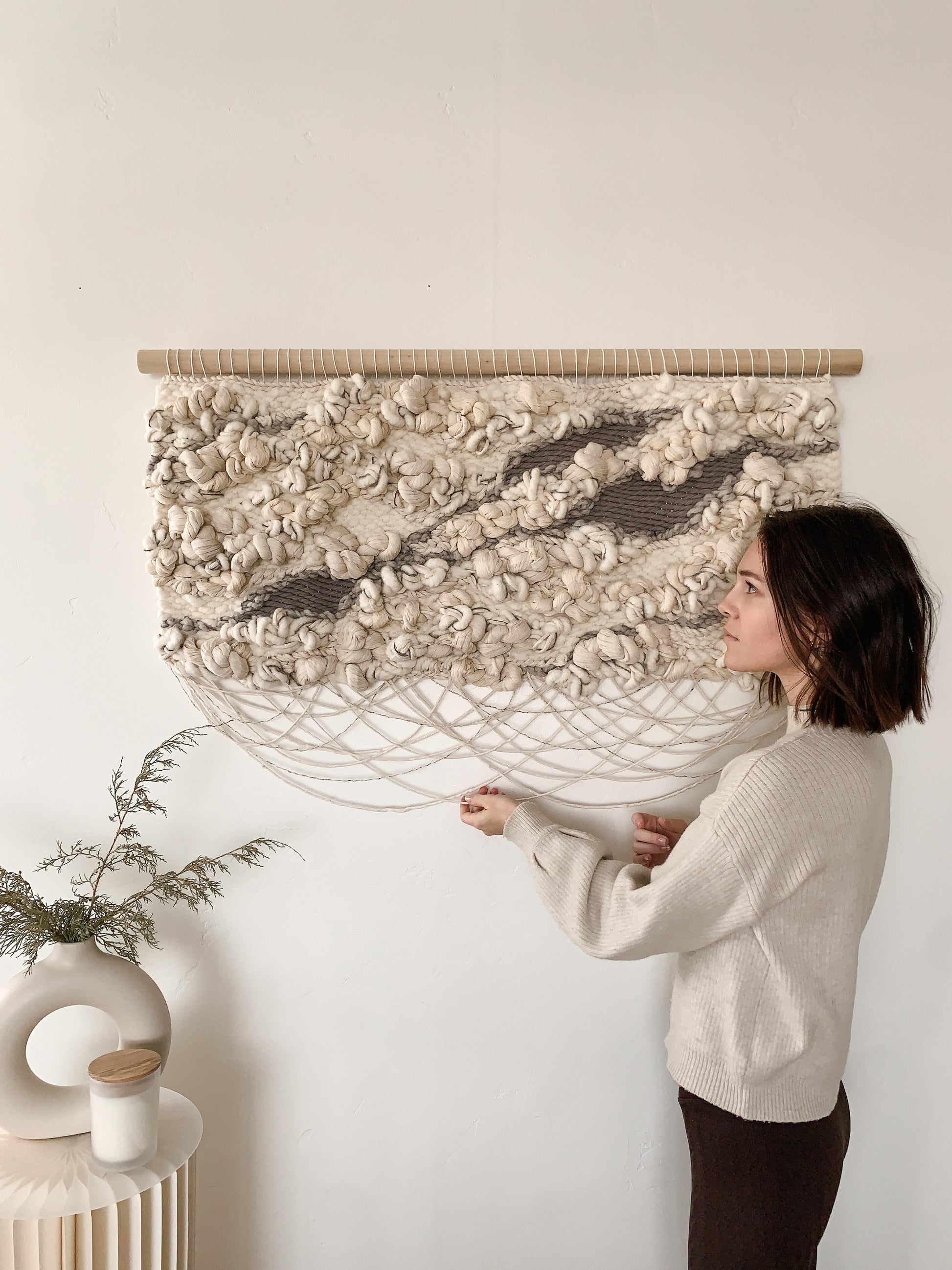 Organic fiber wall art piece utilizing natural wool and cotton, exuding warmth and tactile appeal. Knotted textures with crossing fringe.
