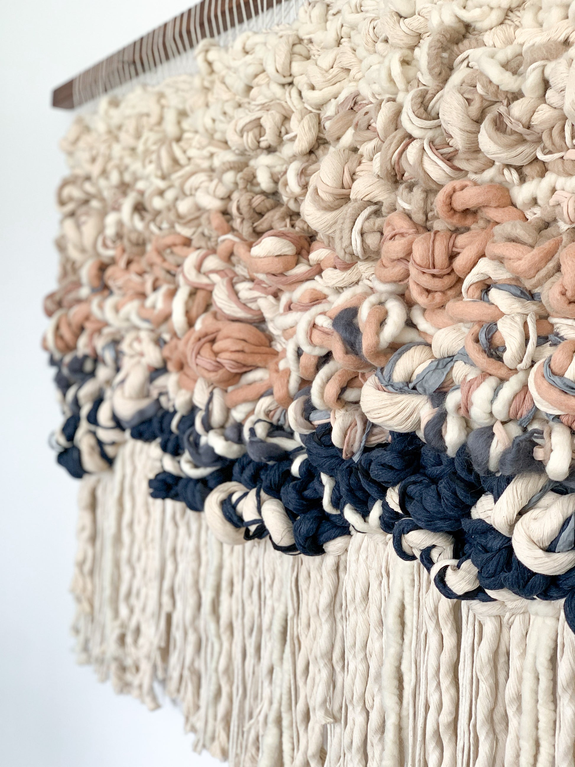 Handcrafted woven tapestry with intricate knotting techniques, creating a dynamic visual centerpiece. Fringe in beige and woven face in blue, salmon, brown, and beige.