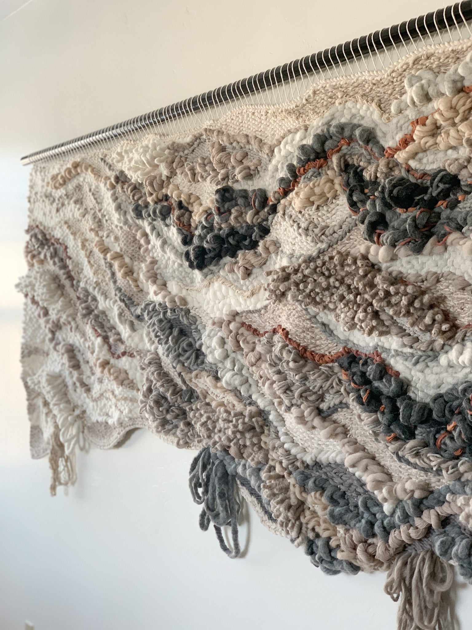 Wool and cotton art piece woven into an abstract landscape-inspired design with rich tactile contrast. Accent colors in burnt orange, slate blue, gray, light browns with beige and ivory.