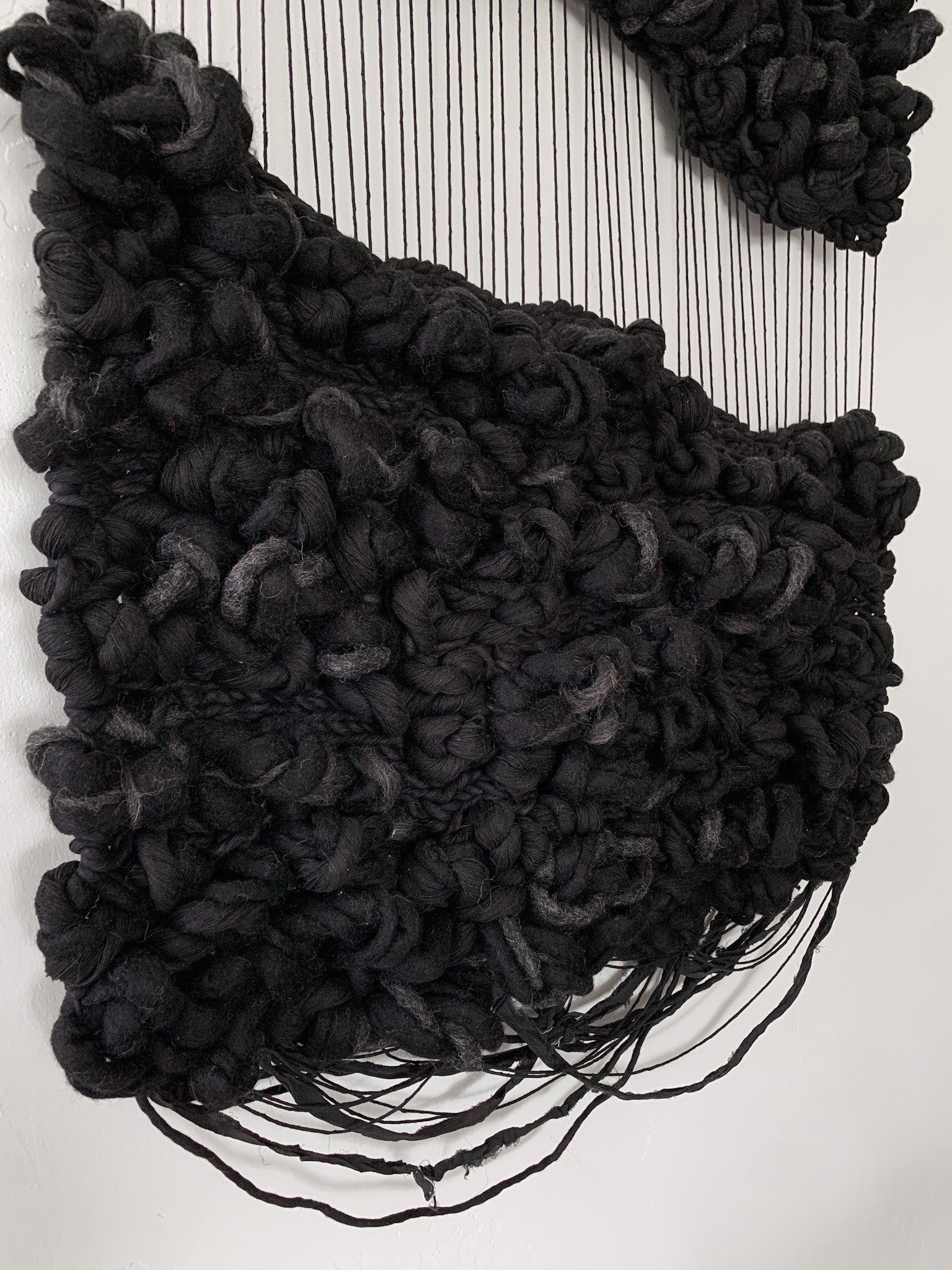 Abstract fiber art tapestry incorporating upcycled materials, reflecting a commitment to sustainable artistry. Knotted woven face with subtle swinging fringe.