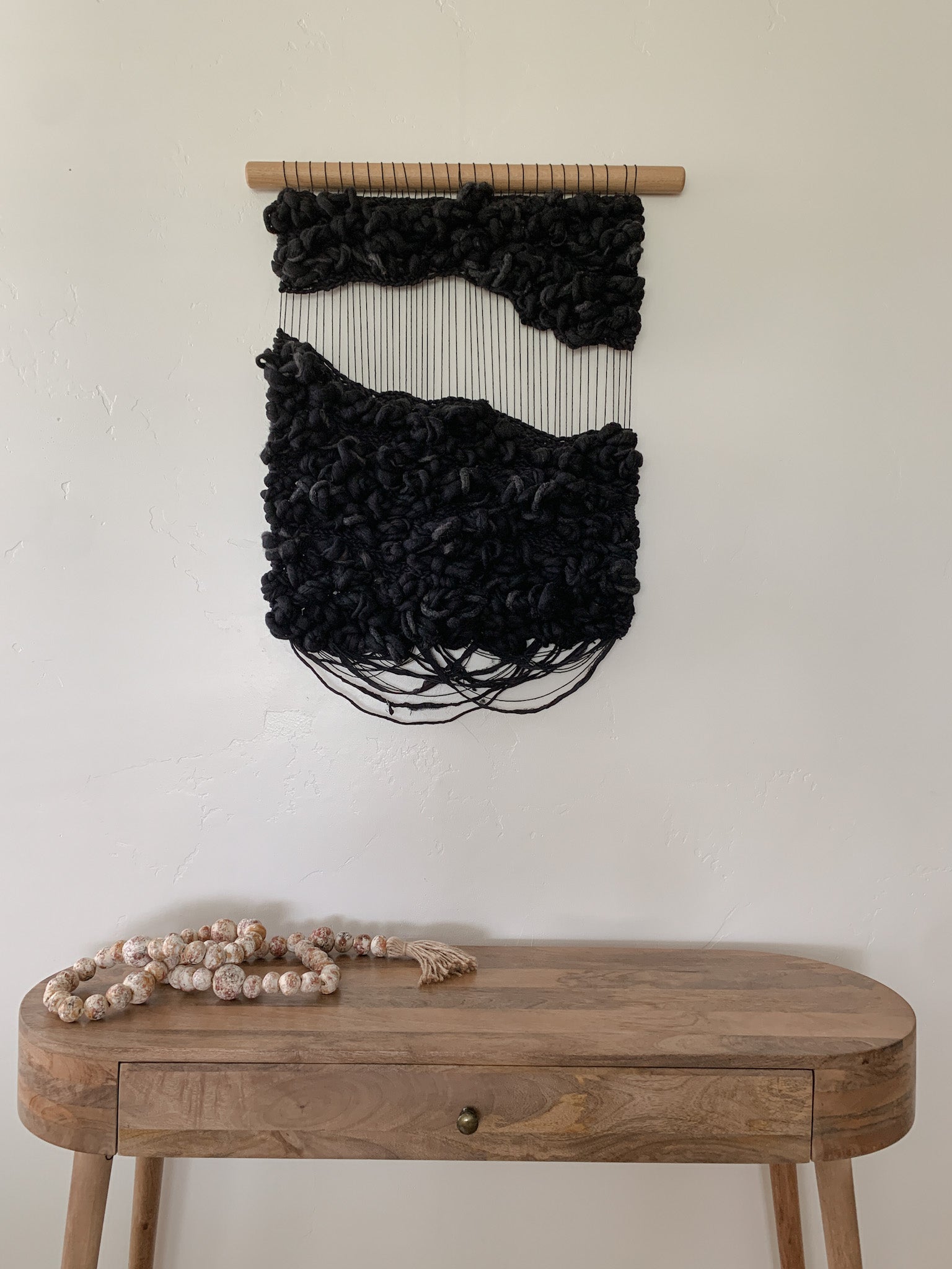 Abstract fiber art tapestry incorporating upcycled materials, reflecting a commitment to sustainable artistry. Accent color in black with subtle fringe and negative space.
