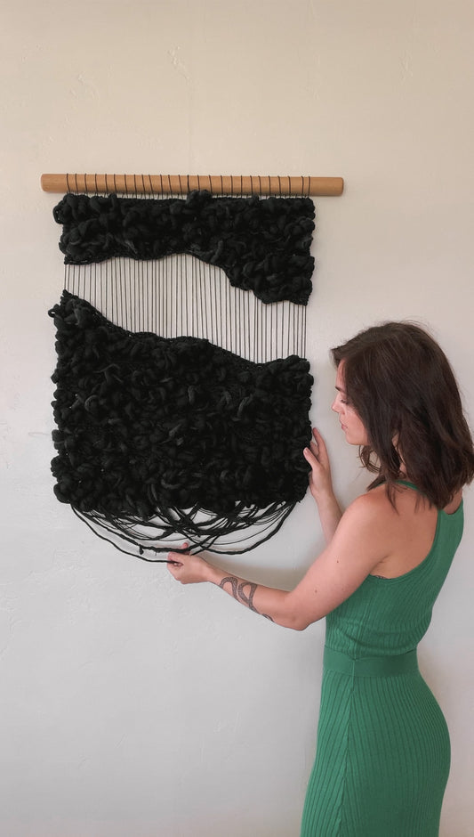 Abstract fiber art tapestry incorporating upcycled materials, reflecting a commitment to sustainable artistry. Negative space with knotted face.