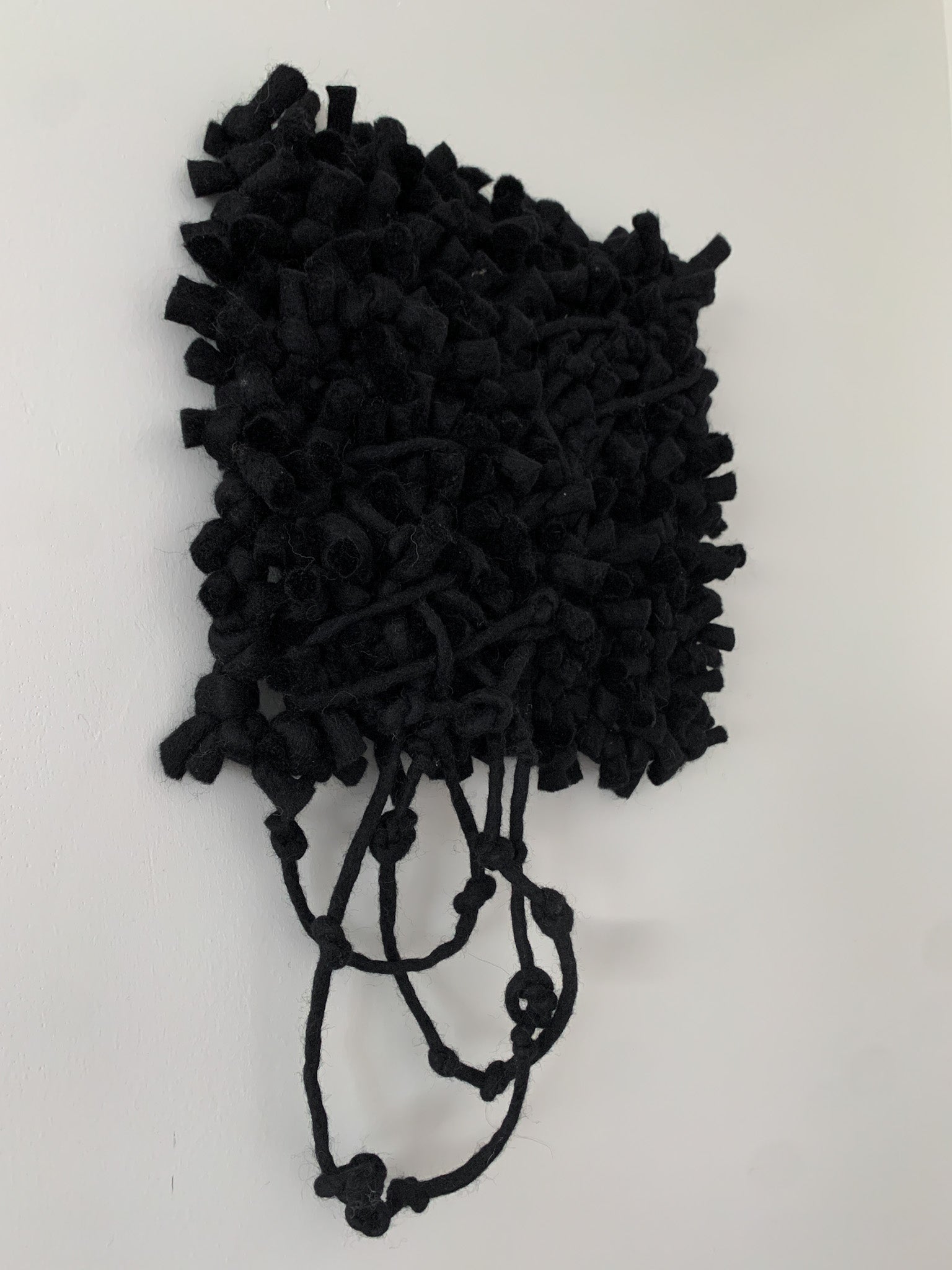 Modern woven wall hanging with asymmetrical design, blending various fiber textures for a unique aesthetic. Knotted fringe and face, with crossing threads.