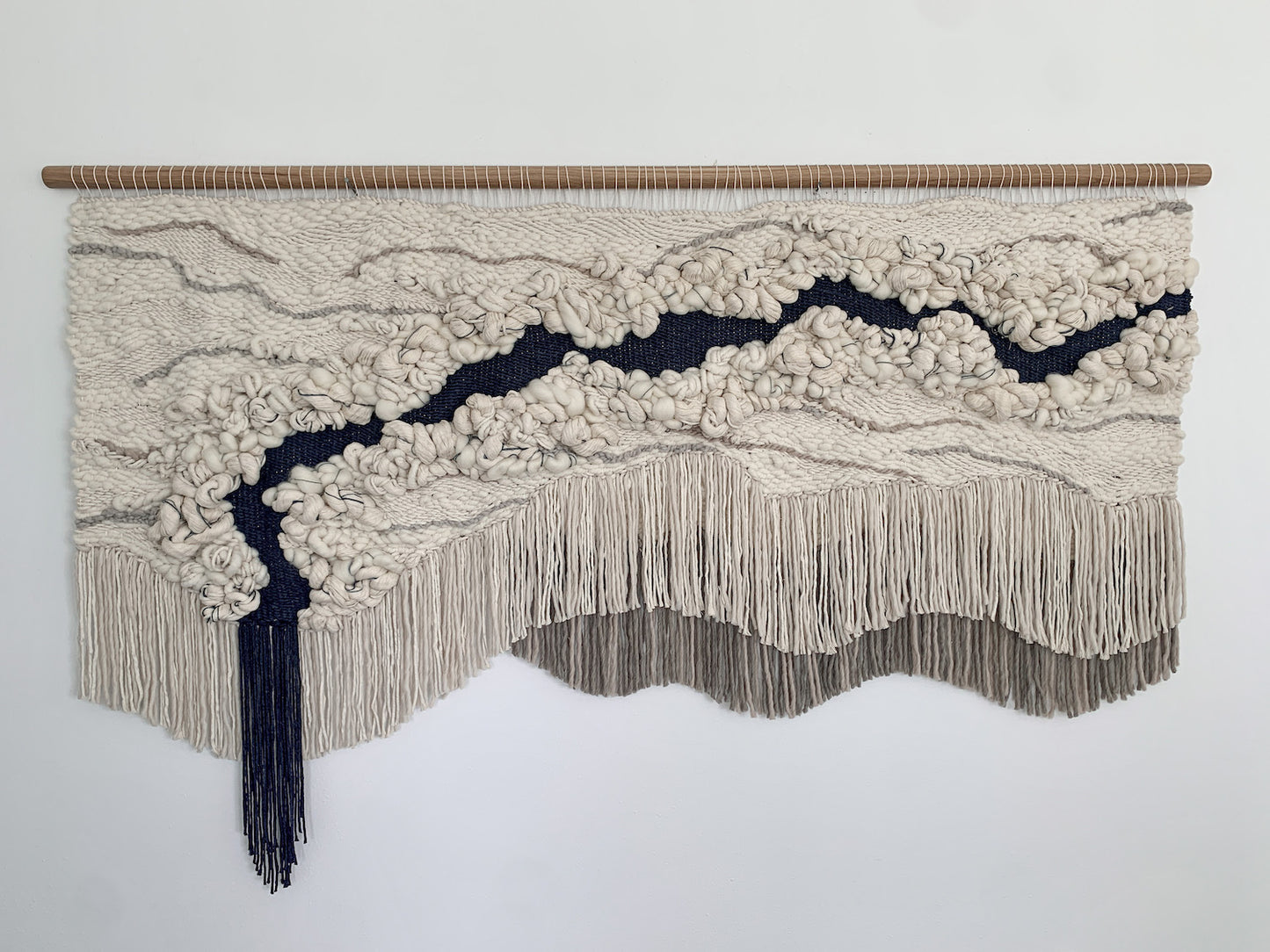 Minimalist fiber art tapestry with clean lines and neutral tones, perfect for serene and modern spaces. Accent color in beige tones, gray, and blue.