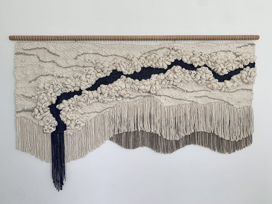 Minimalist fiber art tapestry with clean lines and neutral tones, perfect for serene and modern spaces. Accent color in beige tones, gray, and blue.