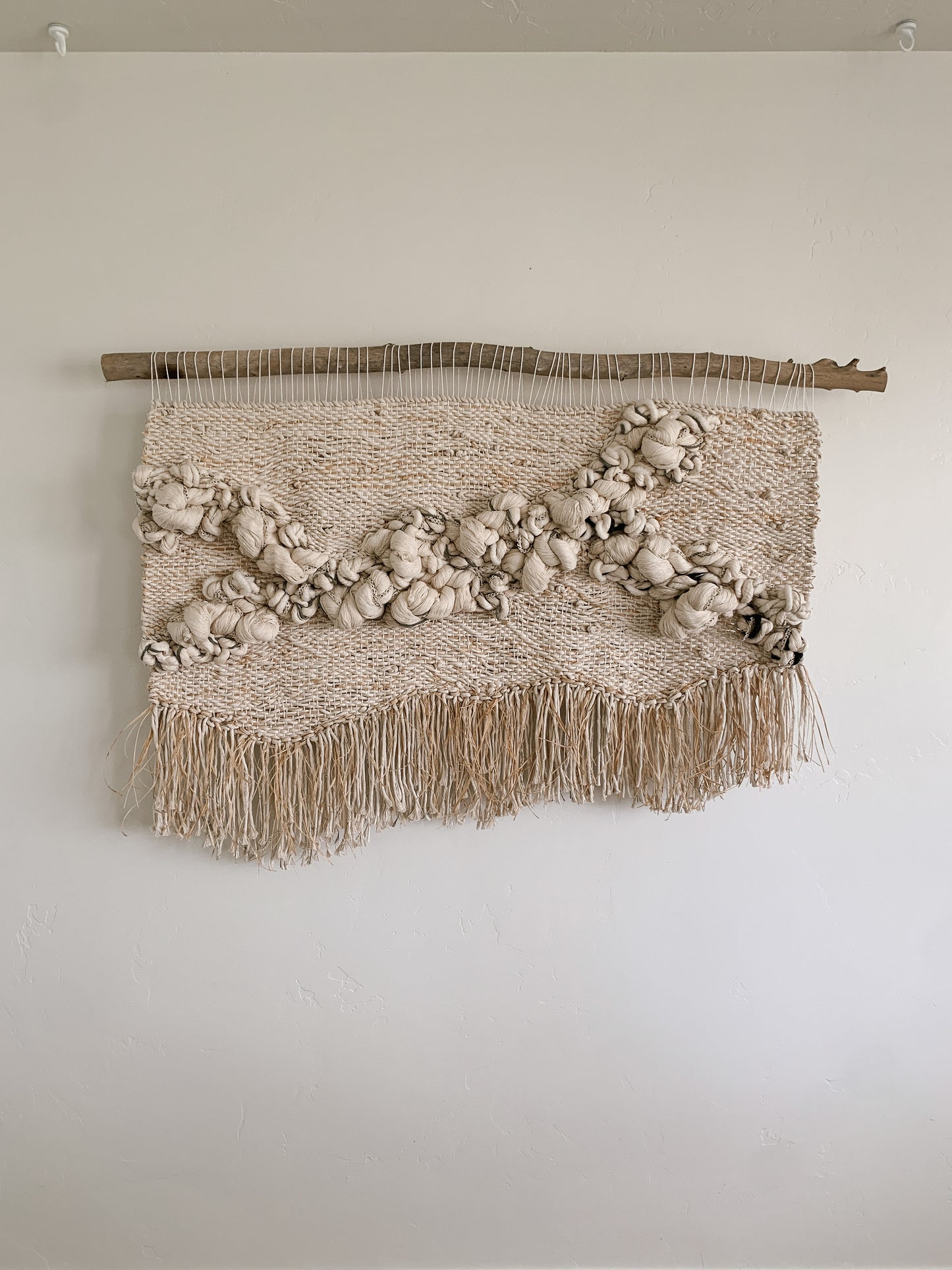 Statement woven wall piece featuring smooth curves and layered fiber work in a calm, monochromatic palette. Knotted texture with organic textured fibers.