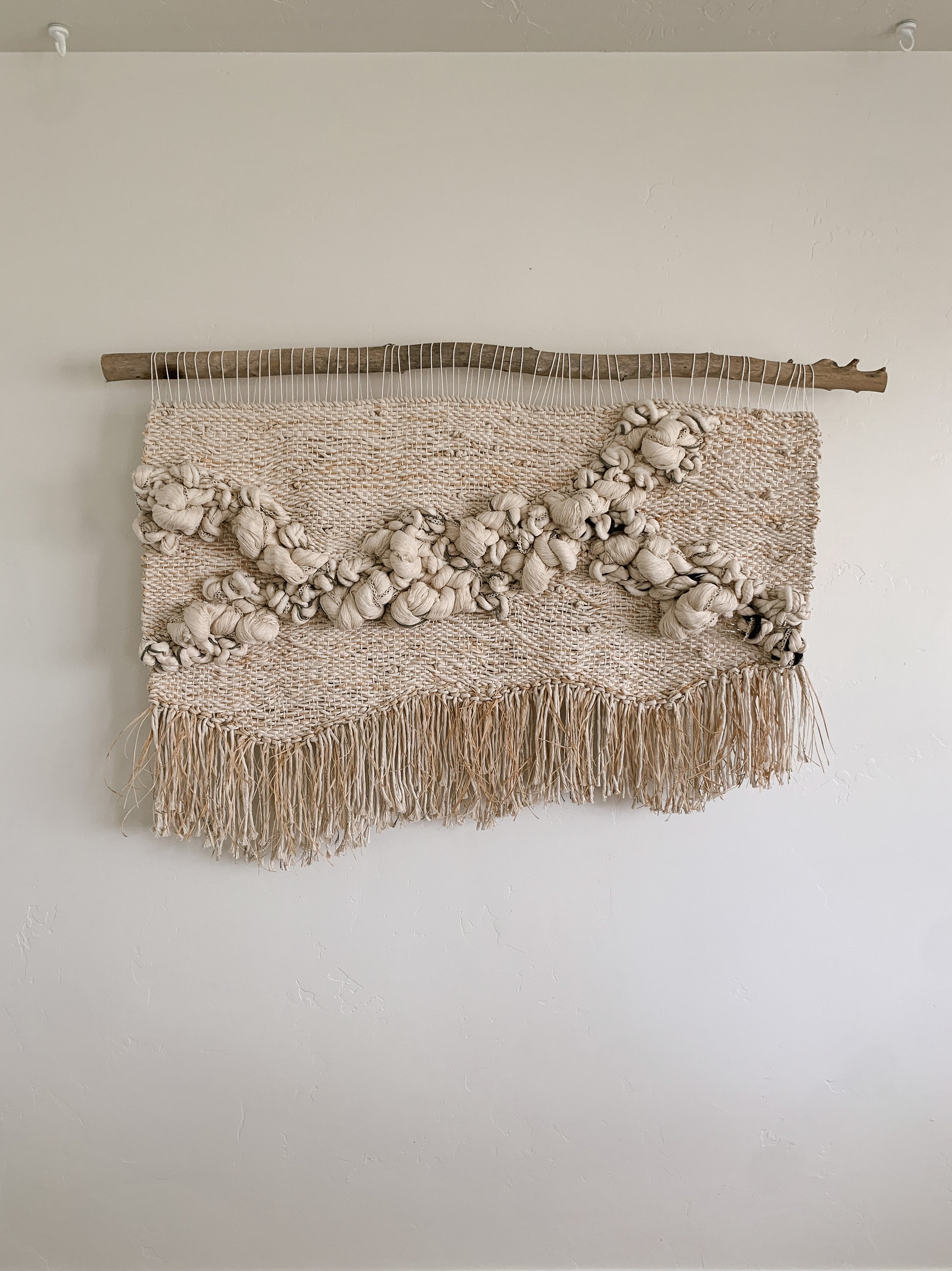 Statement woven wall piece featuring smooth curves and layered fiber work in a calm, monochromatic palette. Knotted texture with organic textured fibers.