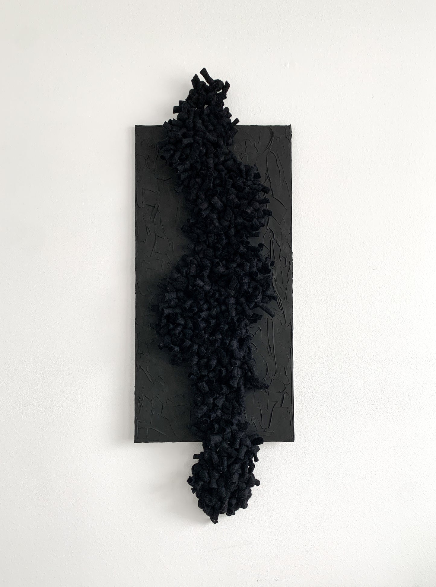 Small black abstract fiber artwork with sculptural texture and layered mixed media elements, combining wool and cotton to create a bold, moody presence in a compact form.
