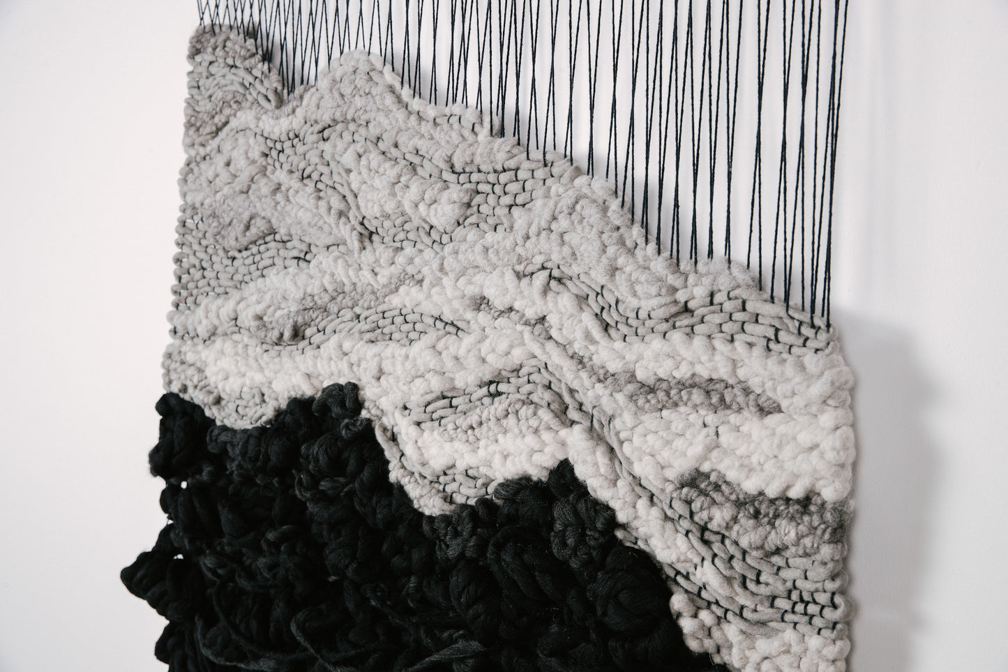 Textile sculpture composed of hand-dyed threads and natural fibers, showcasing organic flow and dimension. Contrasting accents with black, gray and ivory with black hanging threads.