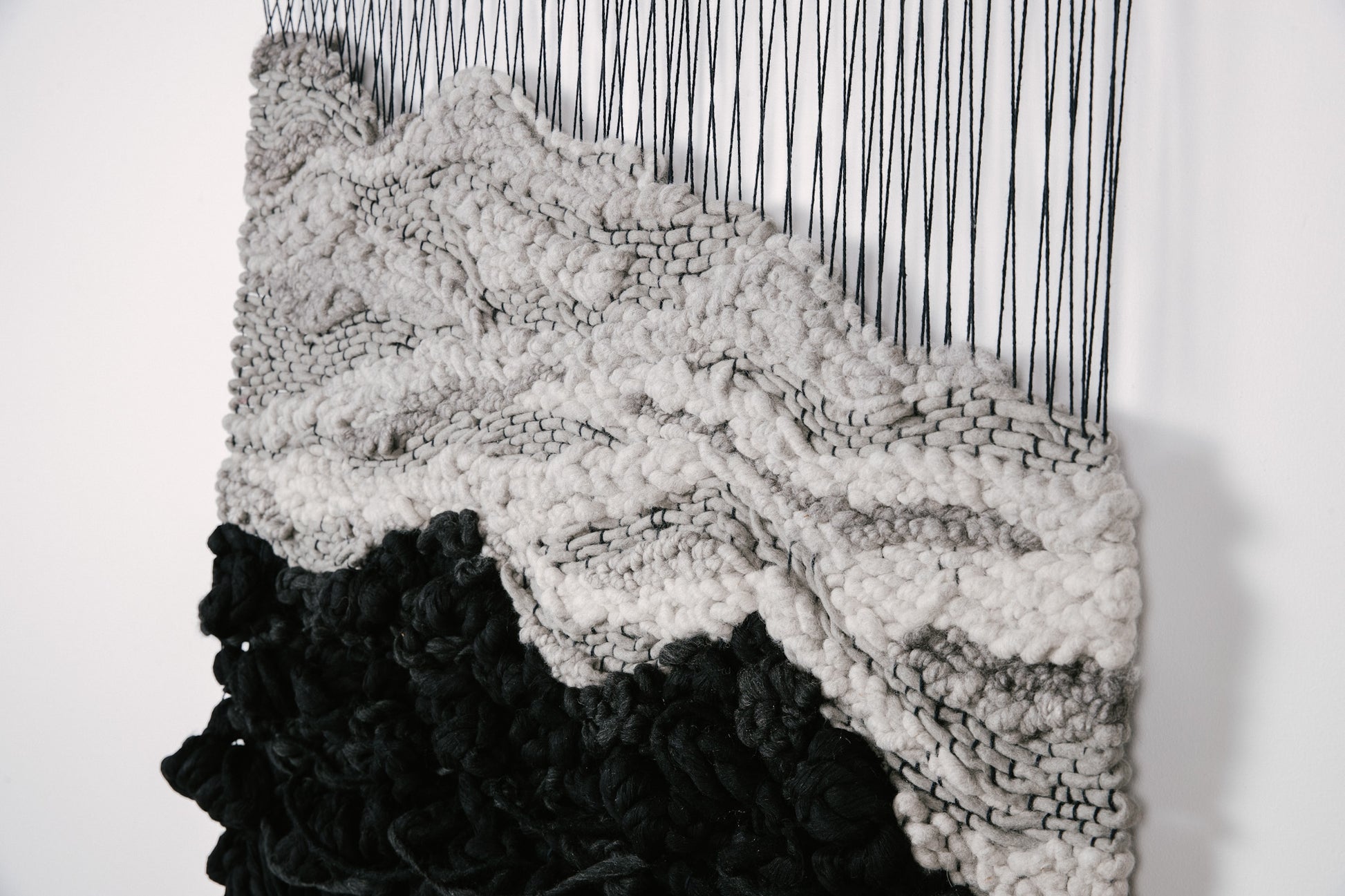 Textile sculpture composed of hand-dyed threads and natural fibers, showcasing organic flow and dimension. Contrasting accents with black, gray and ivory with black hanging threads.