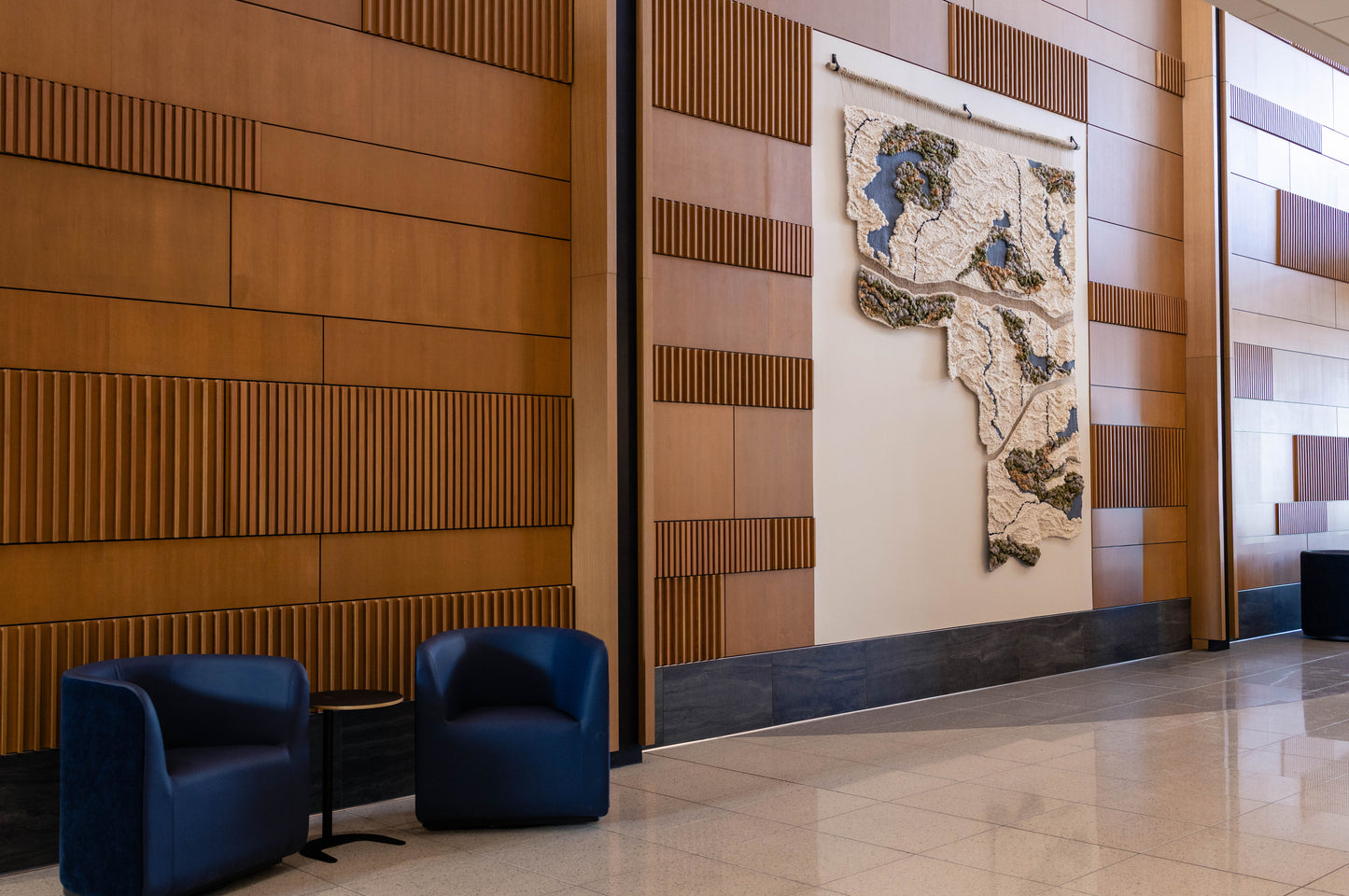 Woven Installation in Modern interior with wooden paneling, blue chairs, and a decorative wall piece.
