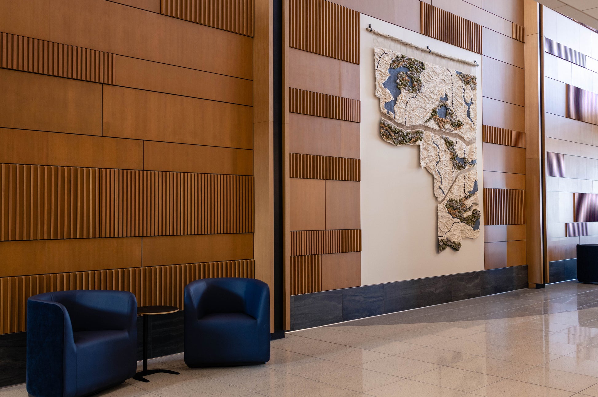 Woven Installation in Modern interior with wooden paneling, blue chairs, and a decorative wall piece.