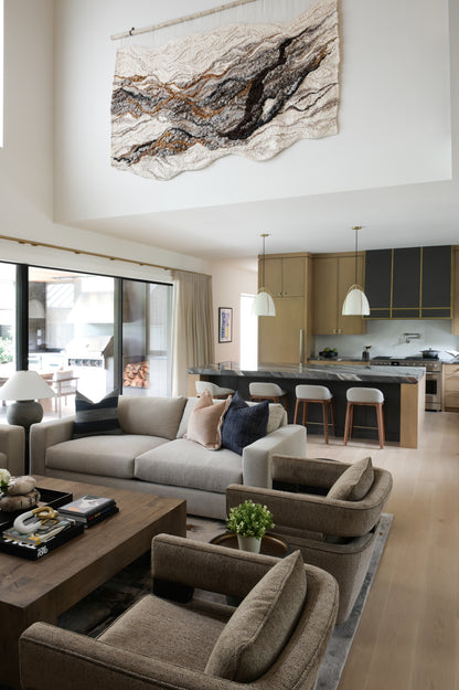 Woven Tapestry in a Modern living room with beige sofa, coffee table, and kitchen in the background.